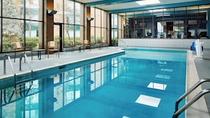 Ein Innenpool mit großen Glaswänden, gefliestem Boden und einigen Liegestühlen.