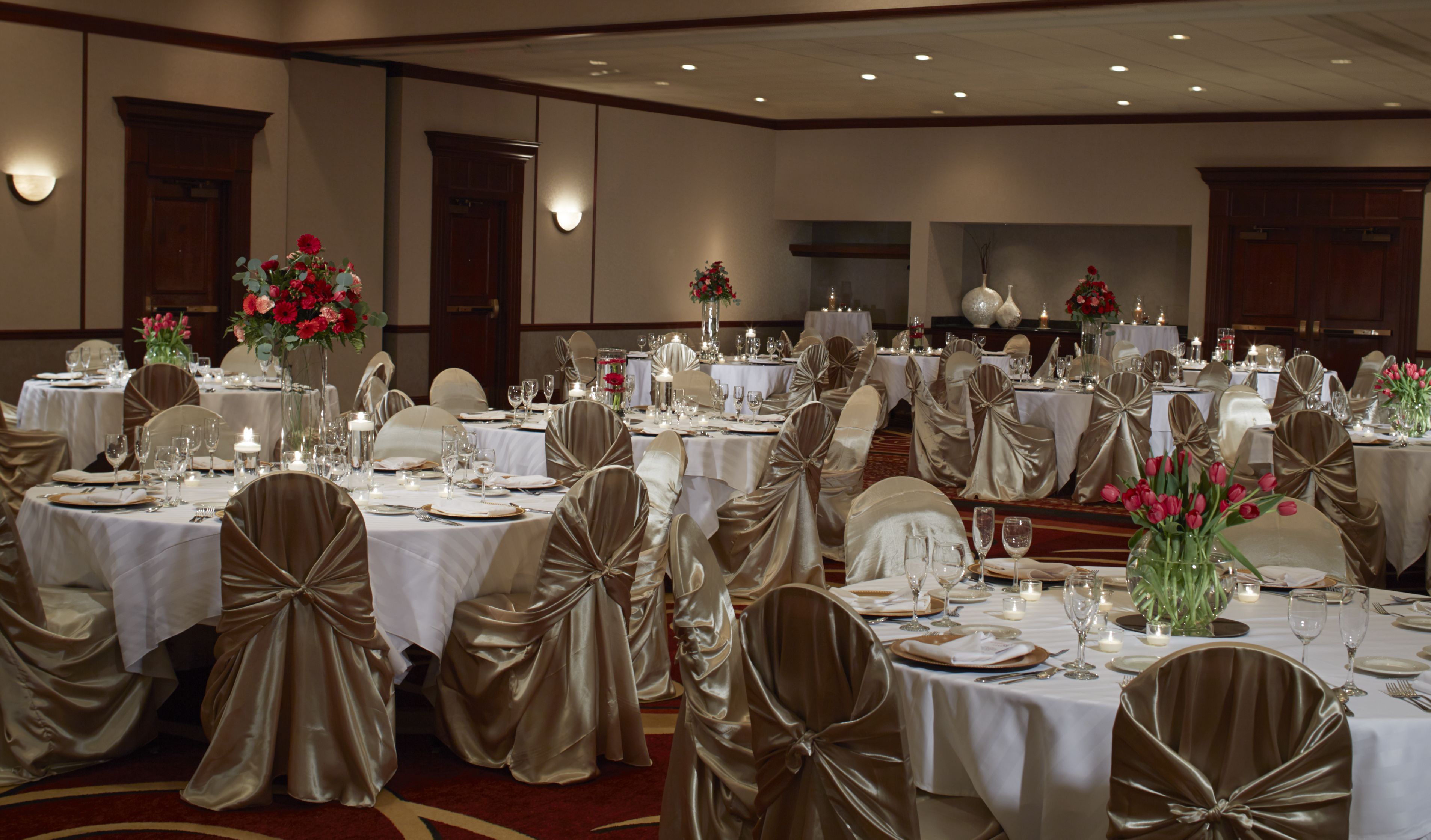 A banquet hall with round tables set for a formal event, featuring white tablecloths, gold chair covers, and floral centerpieces.