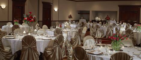 A banquet hall with round tables set for a formal event, featuring white tablecloths, gold chair covers, and floral centerpieces.