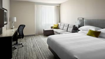 Une chambre d’hôtel avec un grand lit, un canapé, un bureau avec une chaise et une fenêtre avec des rideaux.