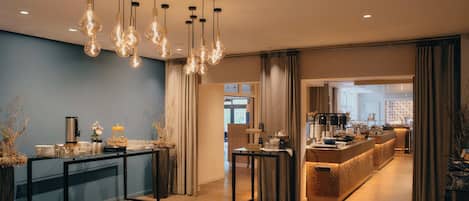 A modern hotel lobby with a reception desk, a coffee station, and a seating area.