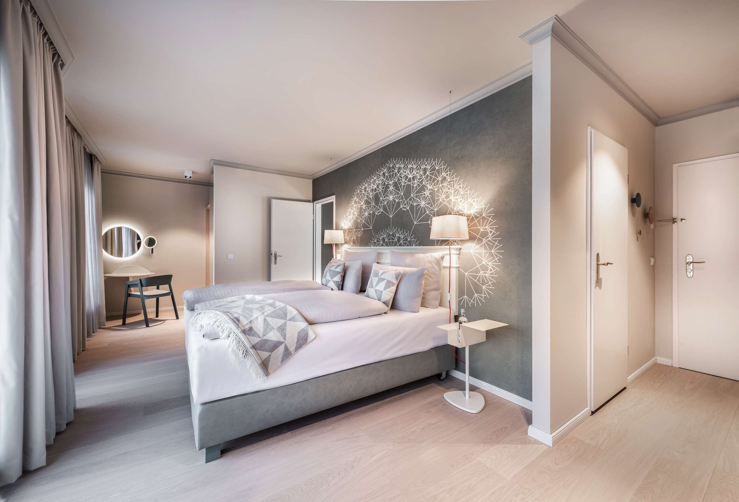 A modern bedroom with a large bed, bedside lamps, a mirror, and a desk with a chair.