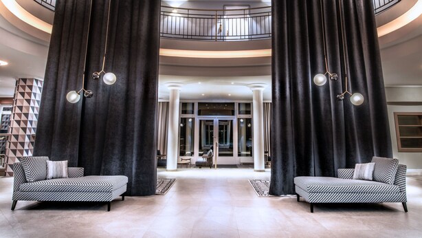 Eine geräumige Lobby mit gewölbter Decke, zwei Sofas und einer Treppe, die zu einer oberen Ebene führt.