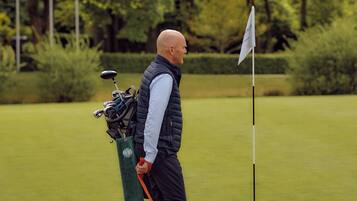 Un hombre pasea un perro en un campo de golf, con un bolso y palos de golf.