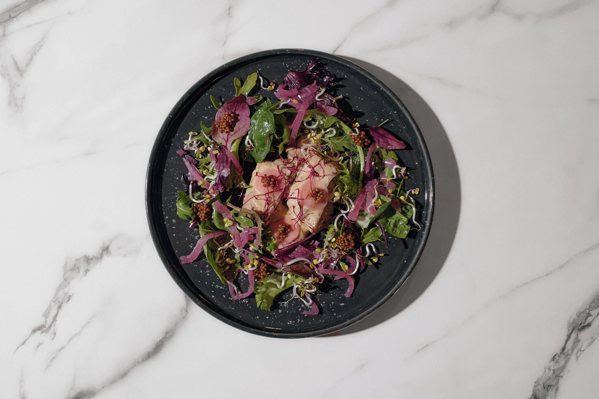 En salat på en sort tallerken med en marmorbaggrund.
