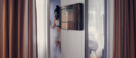 Una habitación de hotel moderna con un ventanal grande, un televisor de pantalla plana montado en la pared y una puerta visible que da a otra habitación.