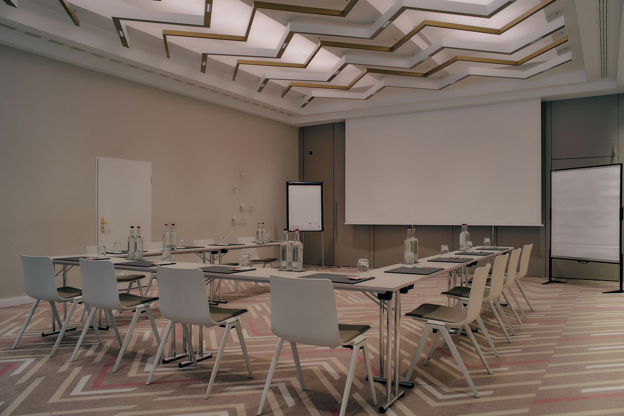 Ein Konferenzraum mit langem Tisch, Stühlen, einer Projektionsleinwand und einer Tafel.
