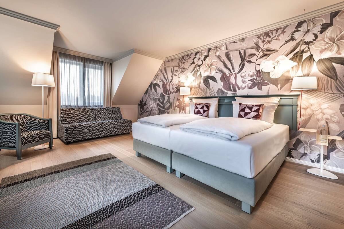 Una habitación de hotel moderna con una cama grande, un sofá, un escritorio y un papel tapiz estampado.