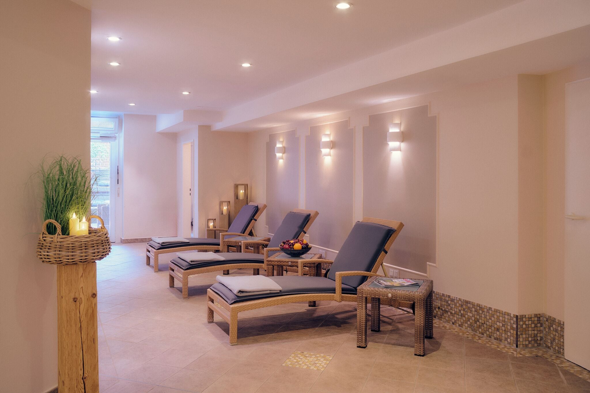 Un espacio de spa con múltiples sillones de relax, una mesita de madera con velas y una silla de mimbre con bandeja.