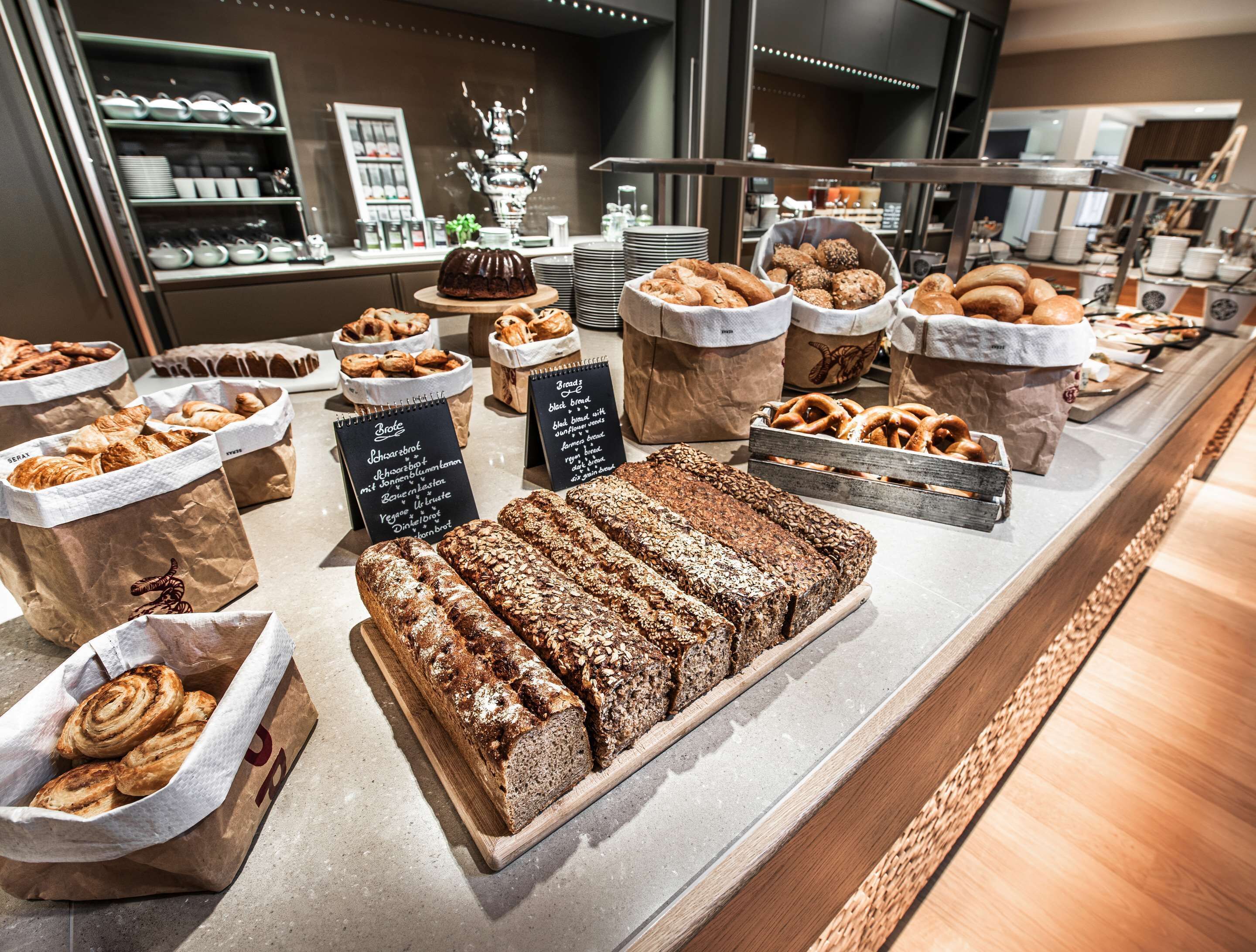 Una vitrina de panadería con panes y pasteles diversos, en bolsas de papel y bandejas de madera.