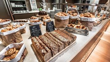 Una vitrina de panadería con panes y pasteles diversos, en bolsas de papel y bandejas de madera.