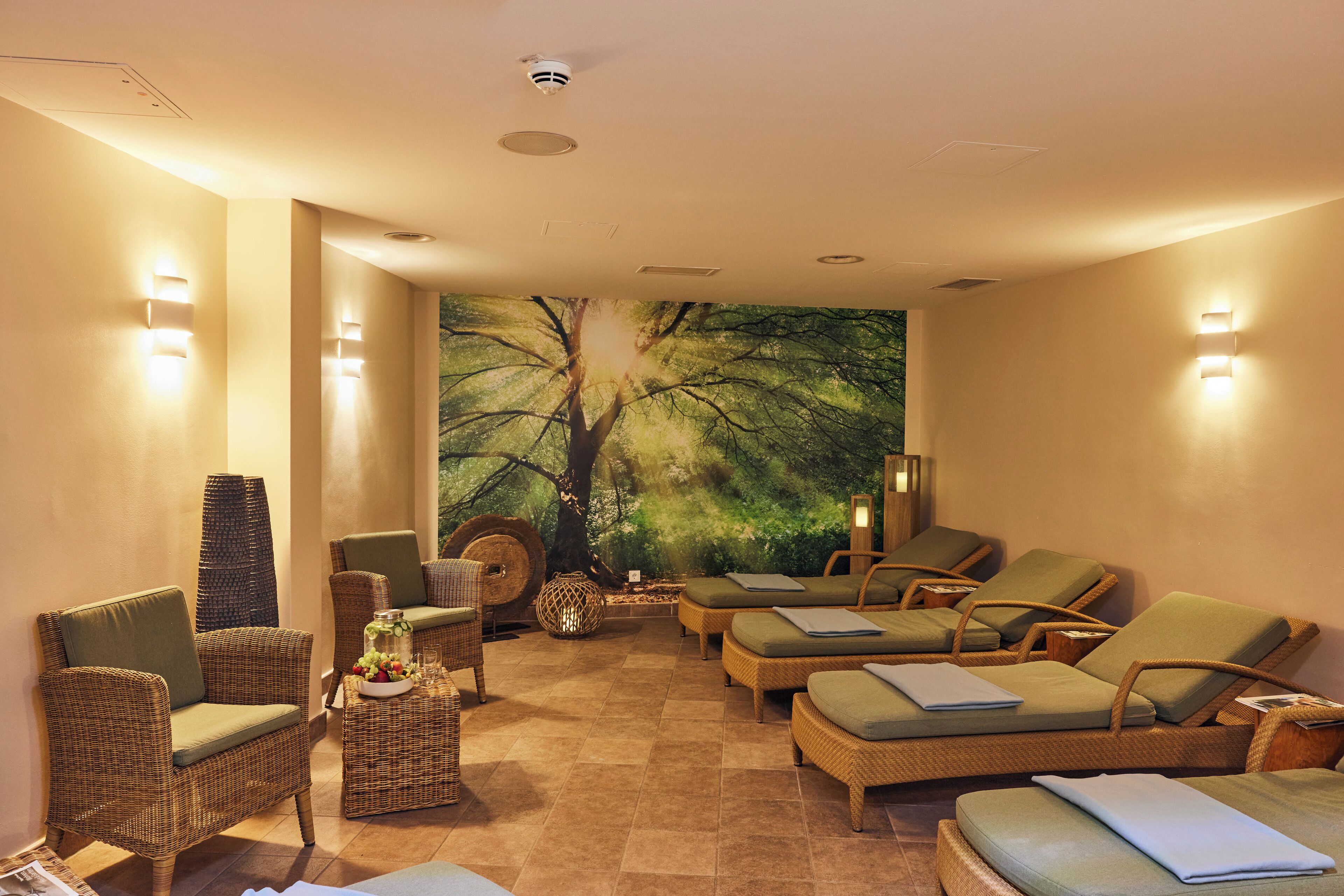 Zona de spa con mobiliario de mimbre, un gran mural de un árbol y luces empotradas.