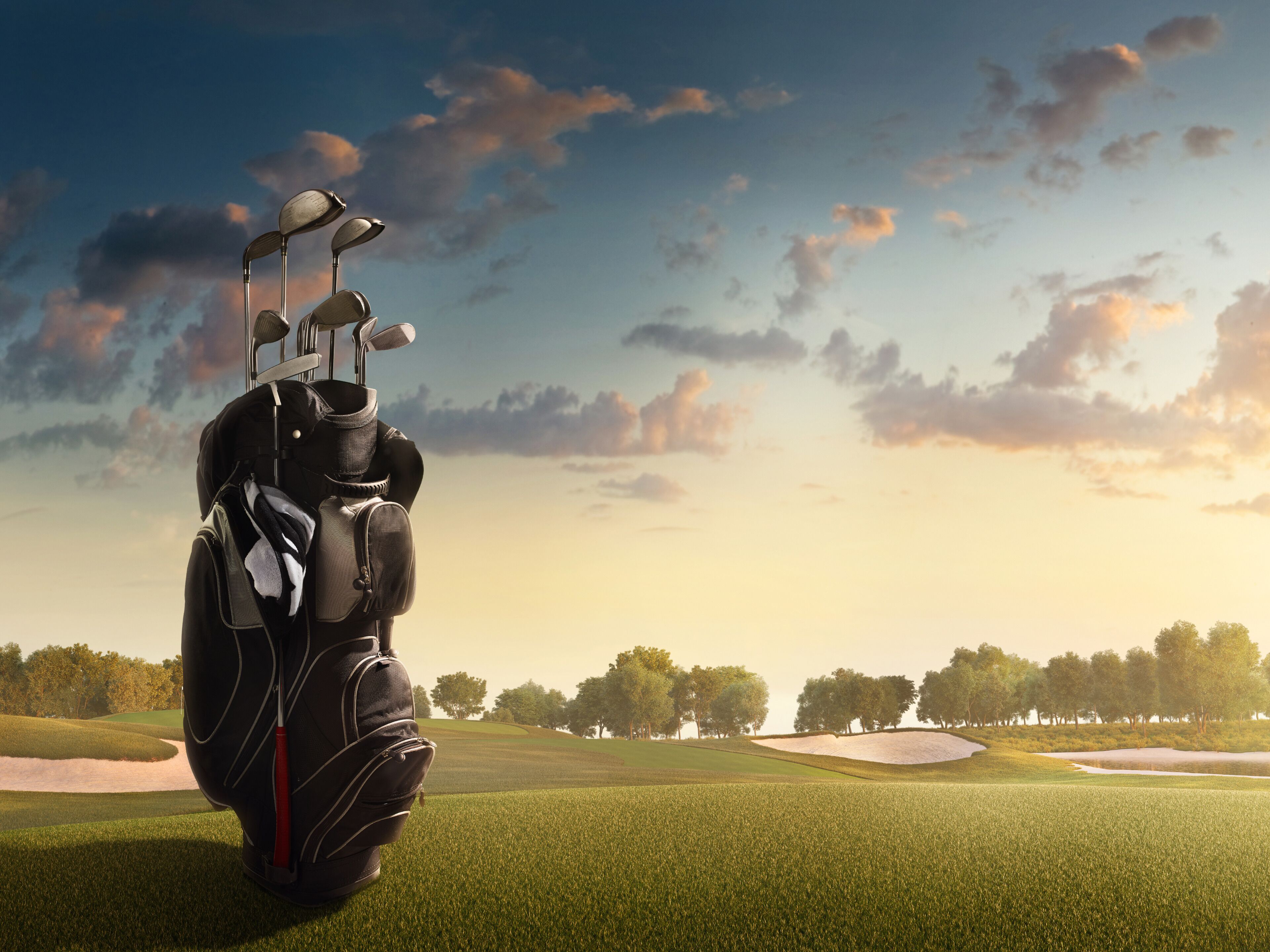 A golf bag with clubs on a golf course with sand bunkers and trees in the background.