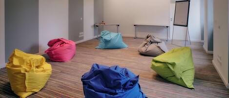 Una habitación con alfombra a rayas, una pizarra y pufs en amarillo, azul y verde.