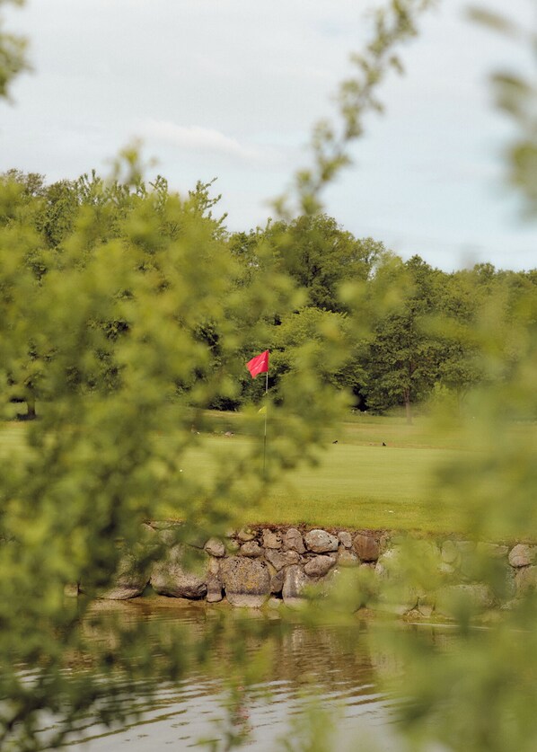 A golf course with a red flag, a pond, and stone walls.