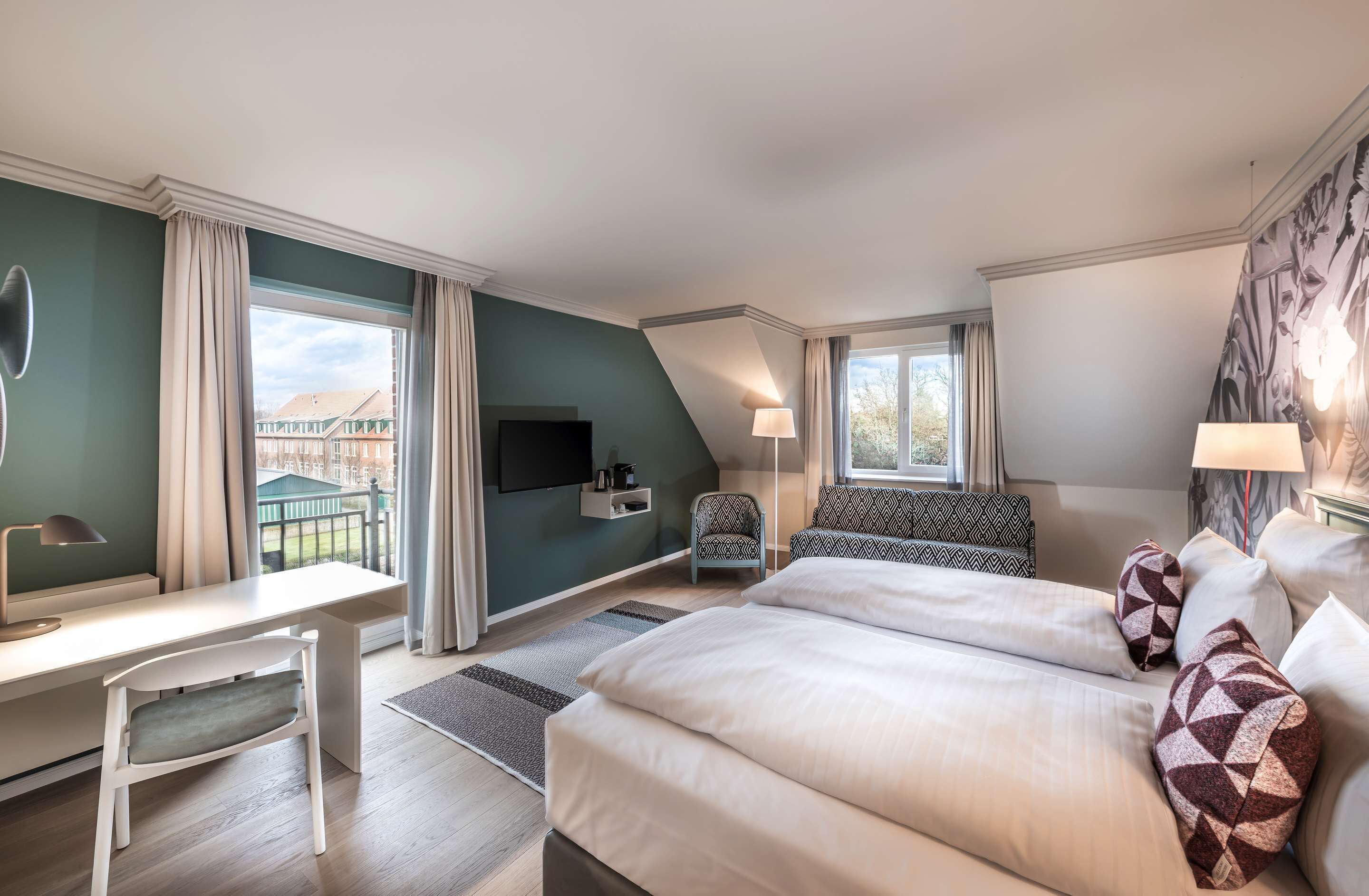Hotelkamer met een groot bed, een bureau met stoel, een aan de muur bevestigde televisie en uitzicht op gebouwen.