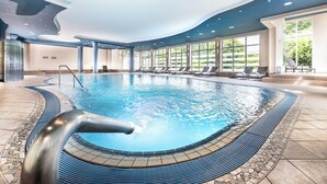 Ein innenliegender Pool mit geschwungener Form, umgeben von Liegestühlen und großen Fenstern.