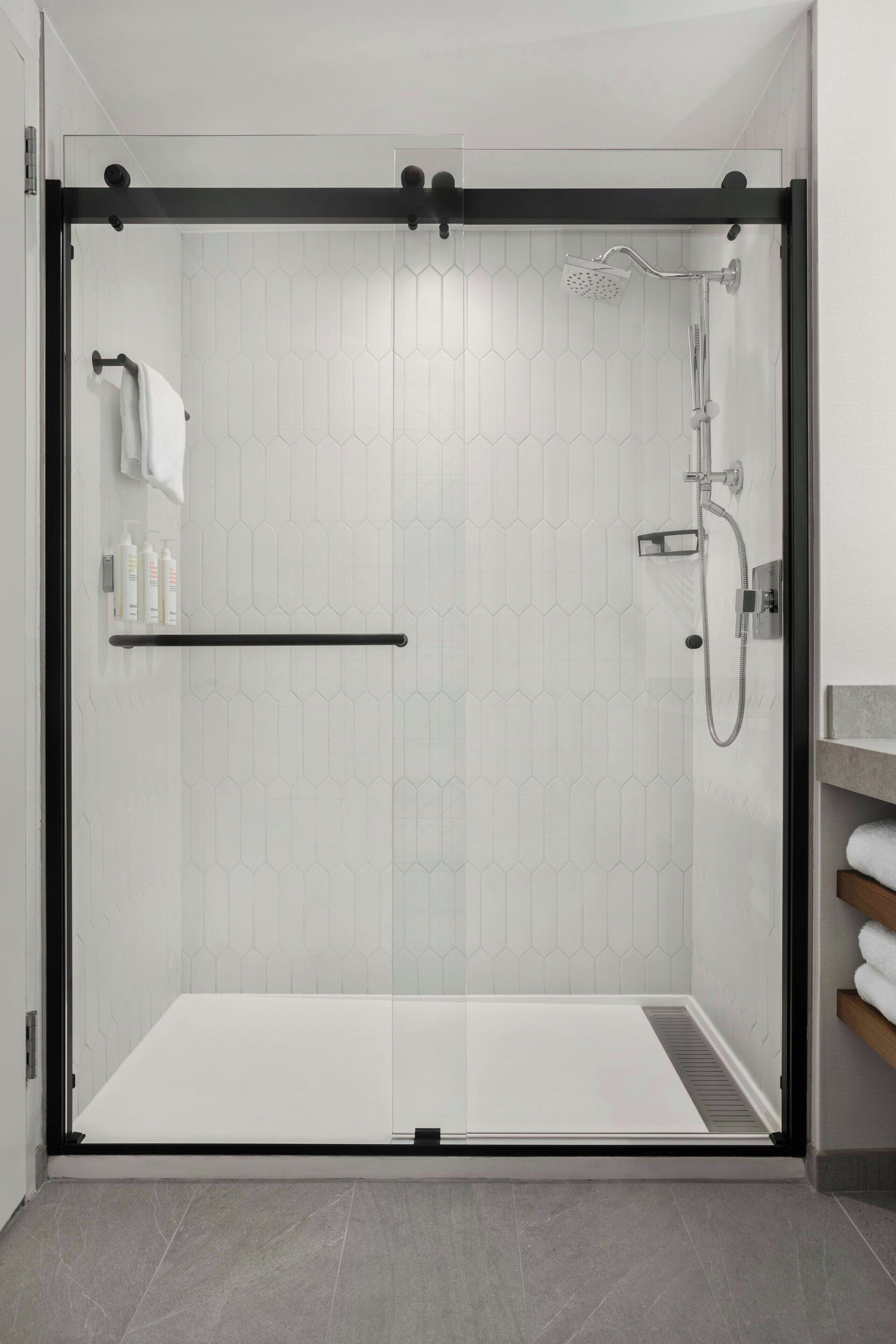 Un box de ducha moderno con puerta de vidrio, un perchero y un cabezal de ducha.
