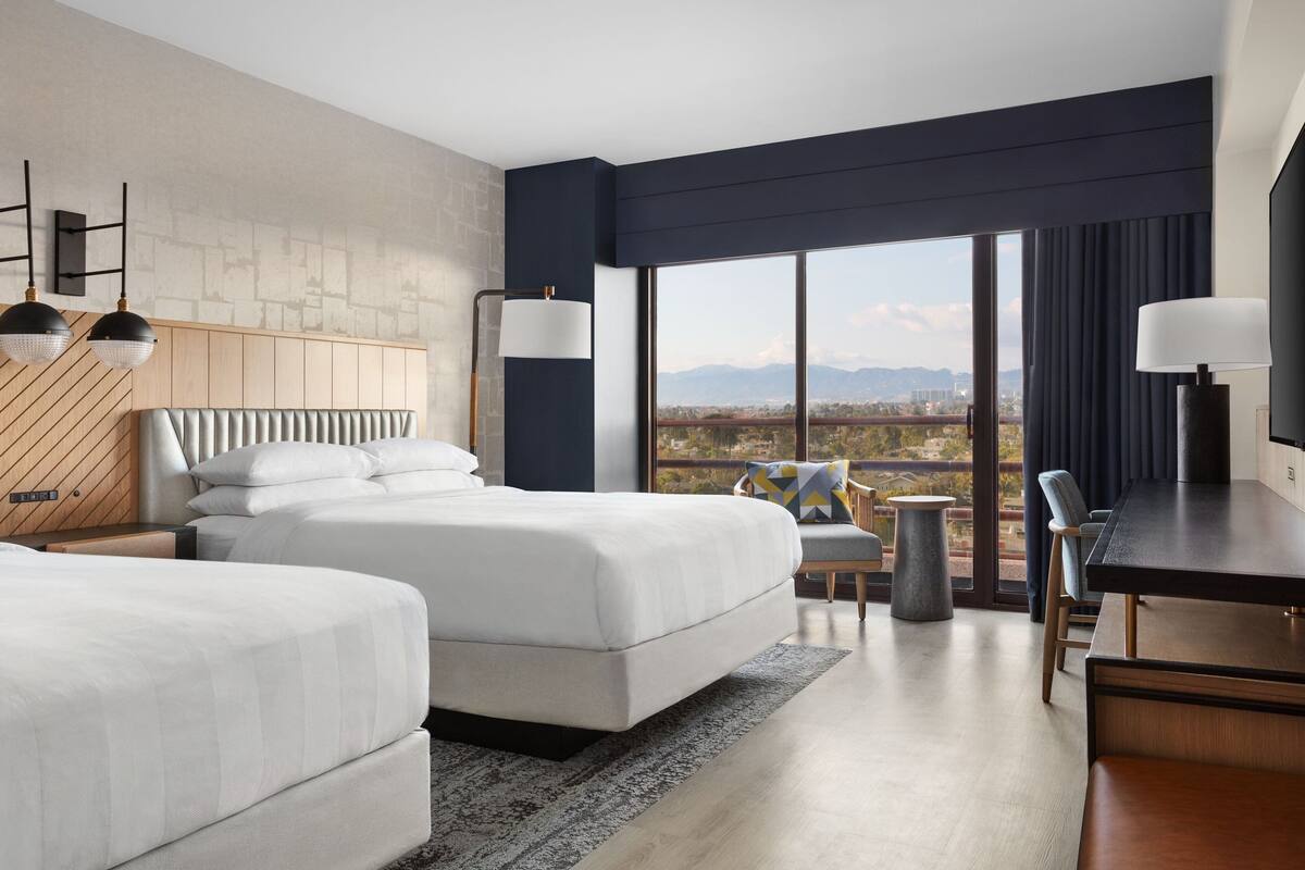 Una habitación de hotel moderna con dos camas, un escritorio y vistas a la ciudad.