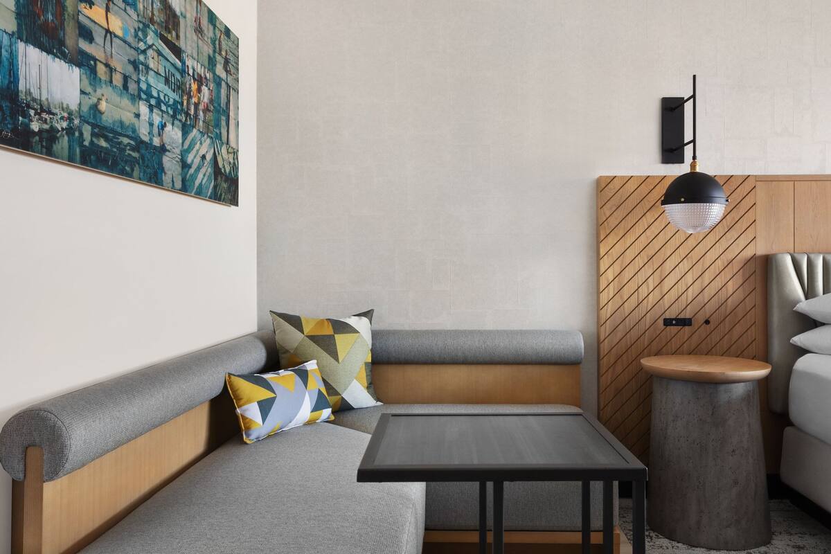 Una sala moderna con un sofá gris, una mesa redonda de madera y una lámpara colgante negra.