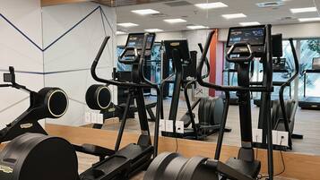 Une salle de sport dotée de nombreux appareils de cardio, notamment des elliptiques et des tapis de course, disposés dans un espace vaste, avec un plancher en bois et de grands miroirs sur les murs.