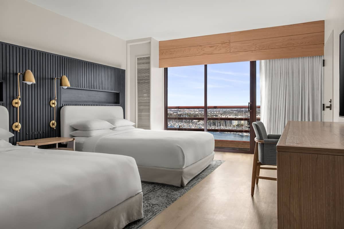 Una habitación de hotel moderna con dos camas, un escritorio y vistas a un puerto deportivo.