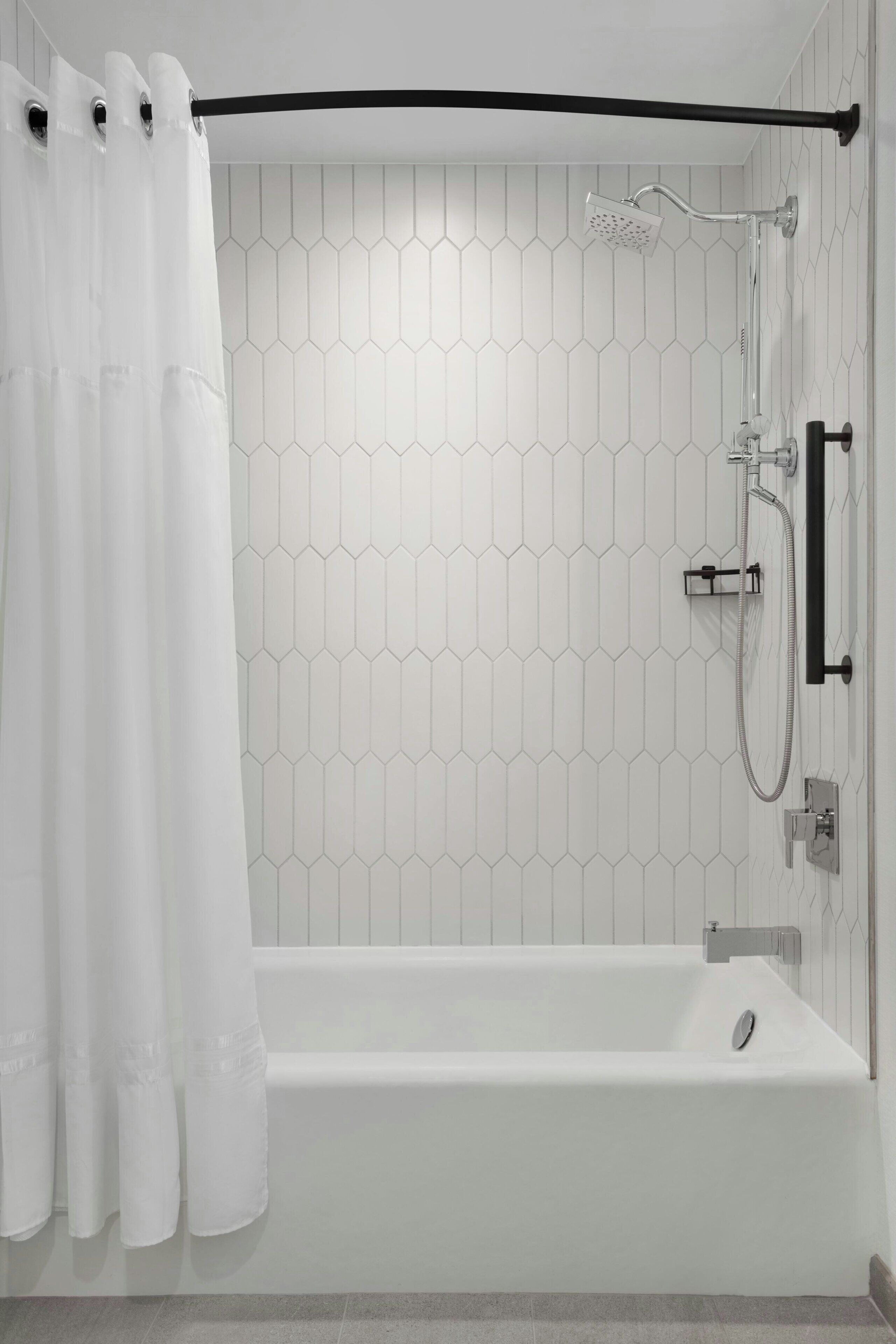 A modern bathroom with a white bathtub, a showerhead, and a black towel bar.