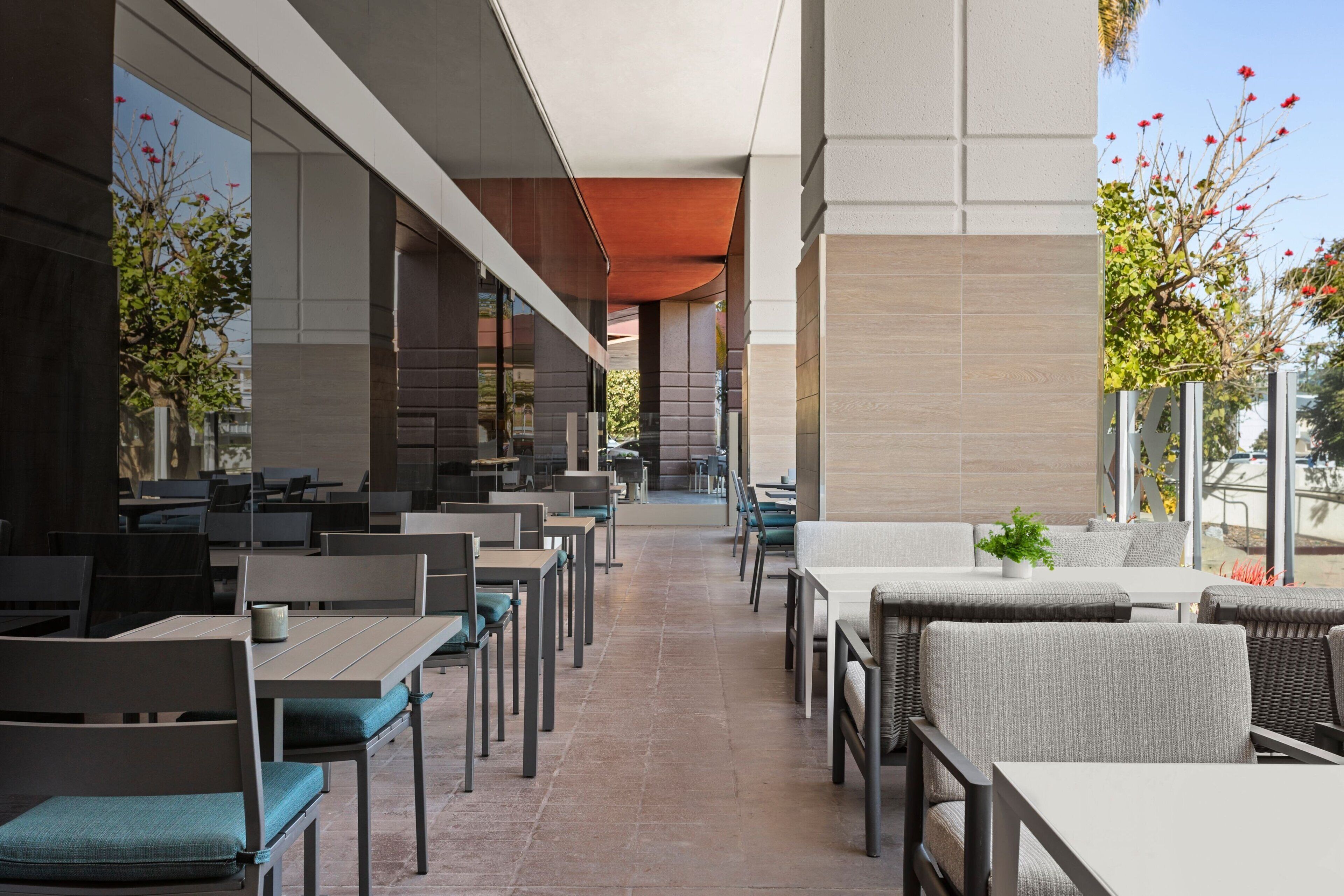 An outdoor dining area with multiple tables and chairs, a clear pathway, and a view of the building's interior.