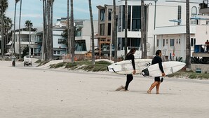 Uma praia com palmeiras e edifícios modernos ao fundo.