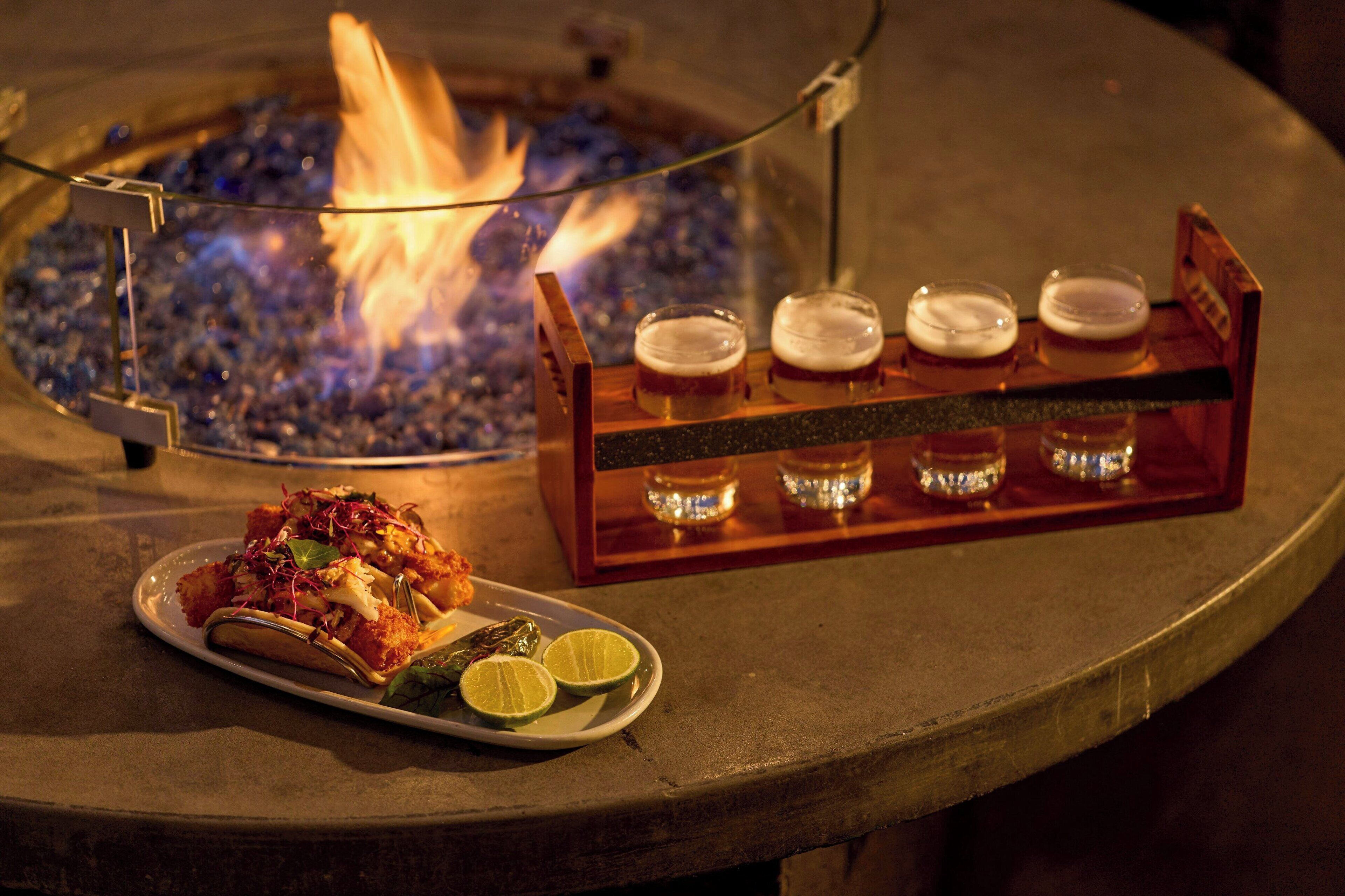 Una mesa con un plato de comida, un juego de bandejas de vidrio con cuatro vasos y una chimenea al fondo.