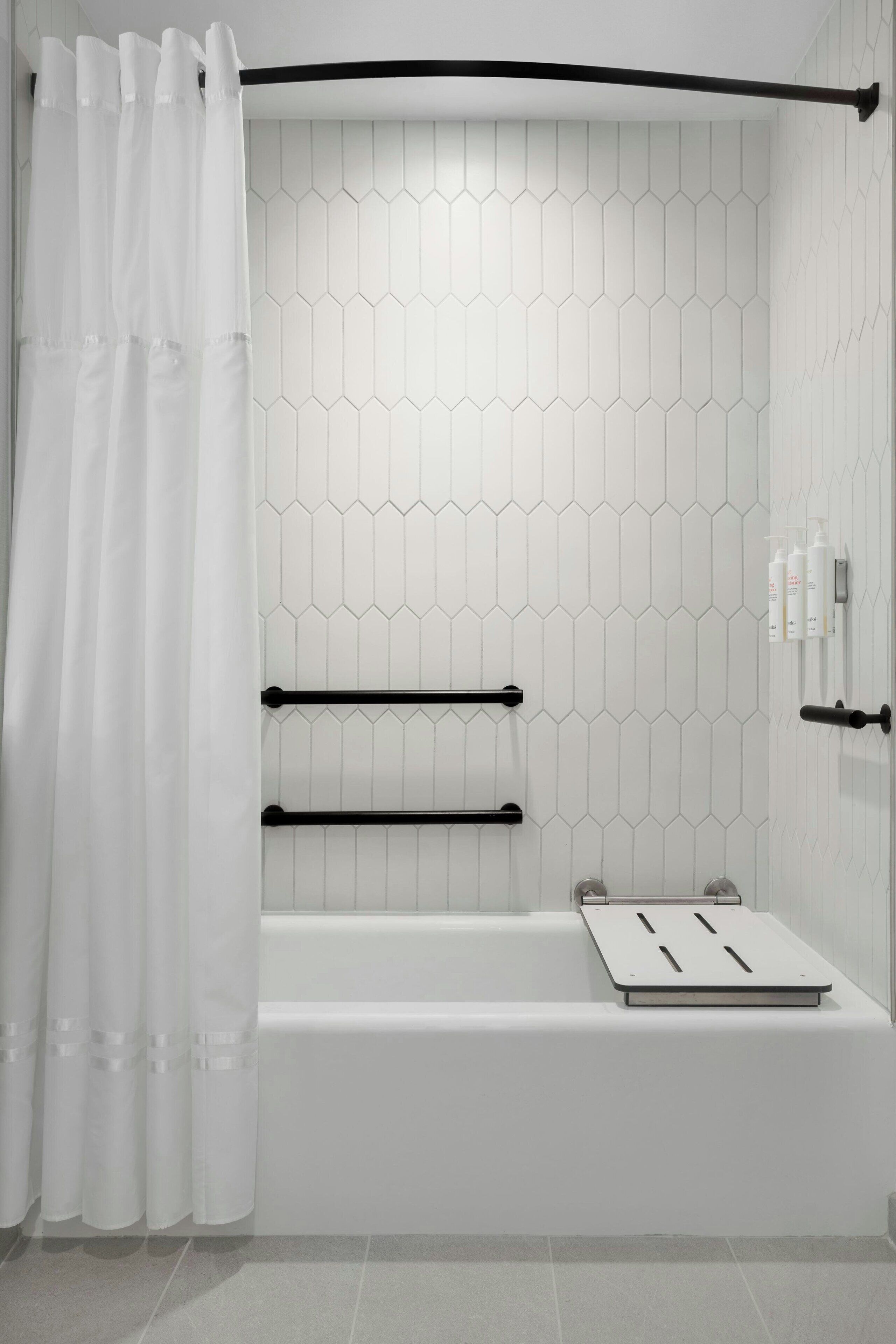 Une salle de bain moderne avec un carrelage blanc disposé en motifs hexagonaux, un porte-serviettes noir et un rideau de douche.