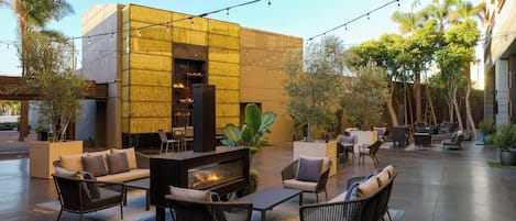 An outdoor seating area with a fire feature, wicker furniture, and a modern building with a textured facade.