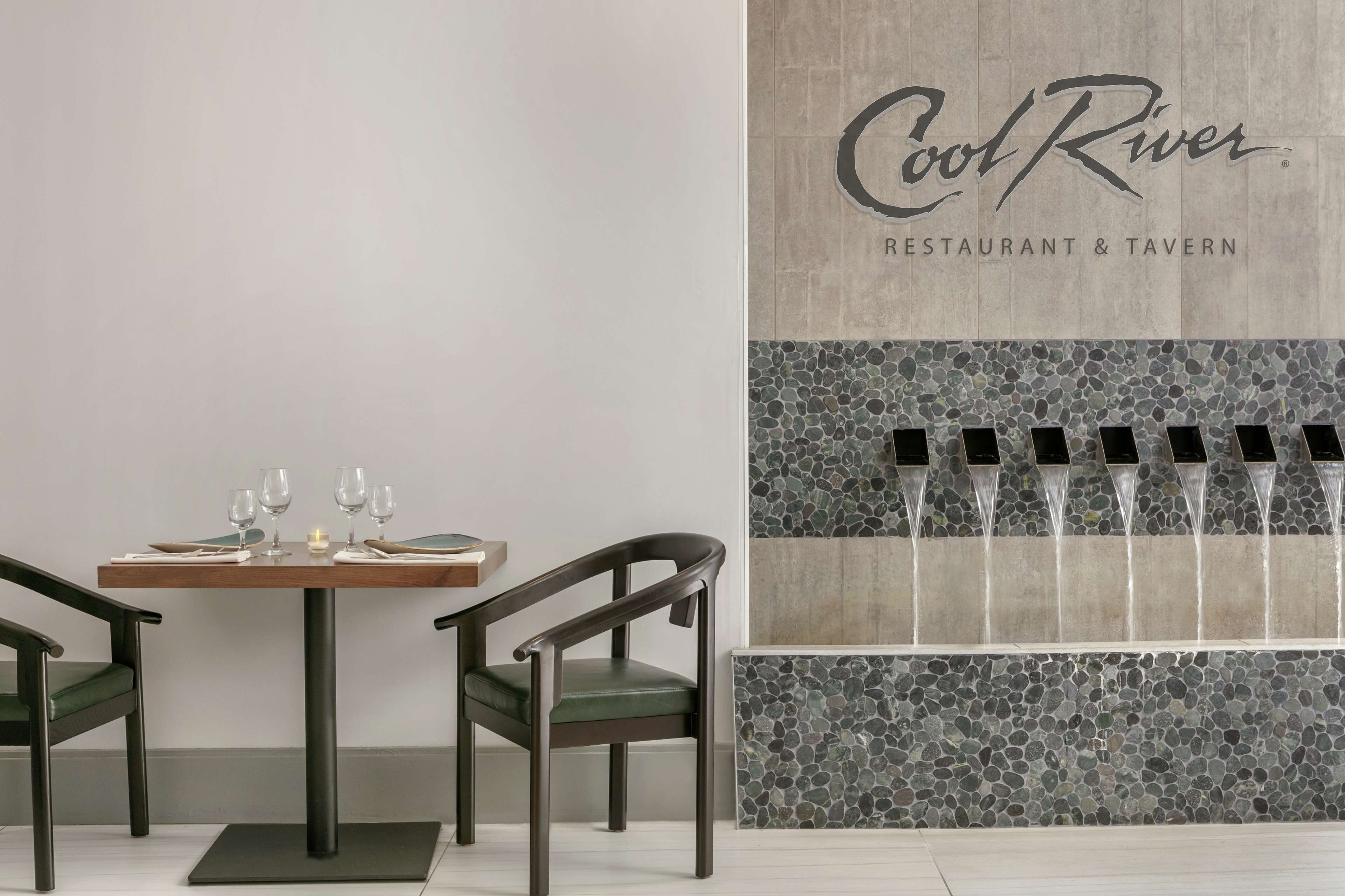 A restaurant interior with a table set for two, chairs, and a wall with a 'Cool River Restaurant & Tavern' sign.