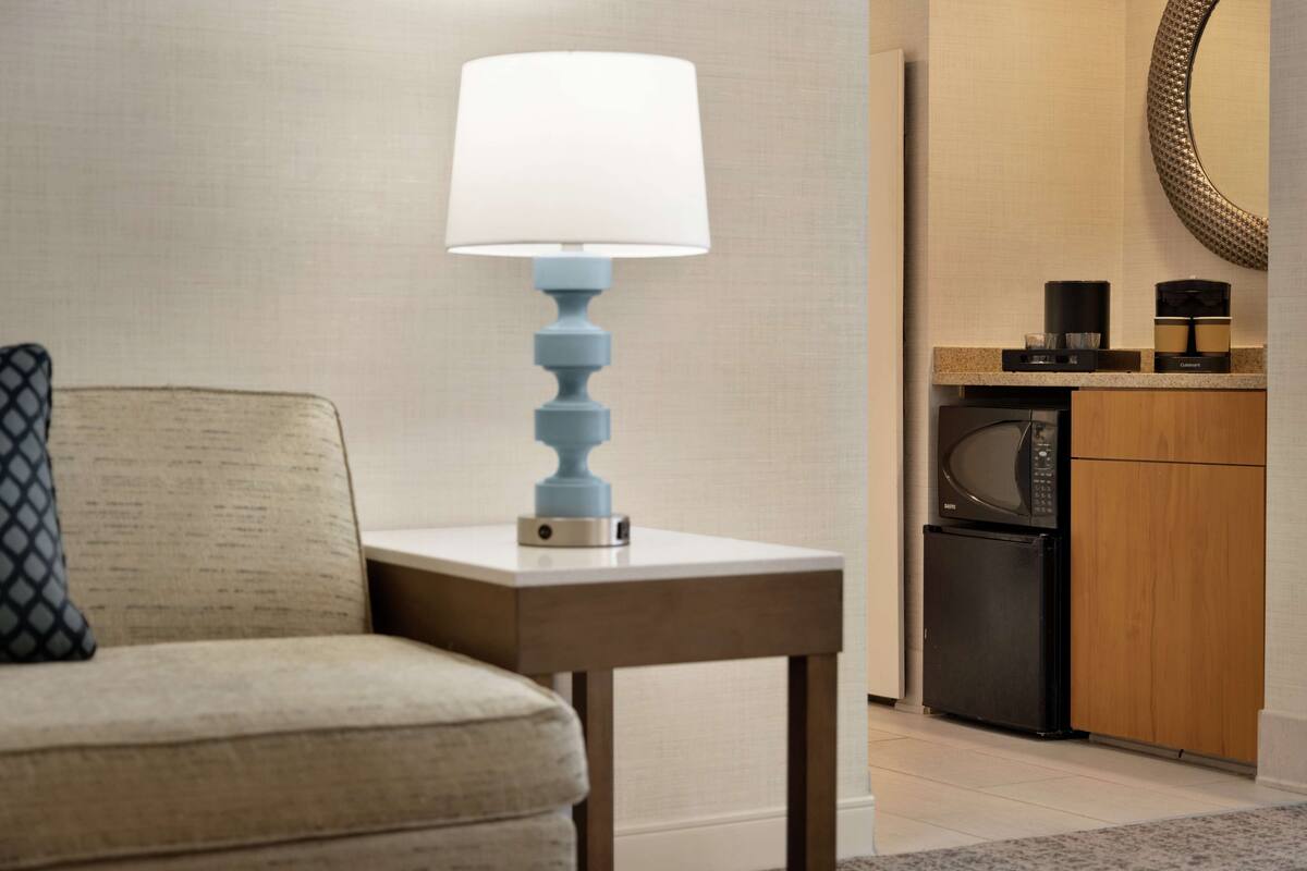 A hotel room with a sofa, a table with a lamp, a microwave, and a coffee maker.