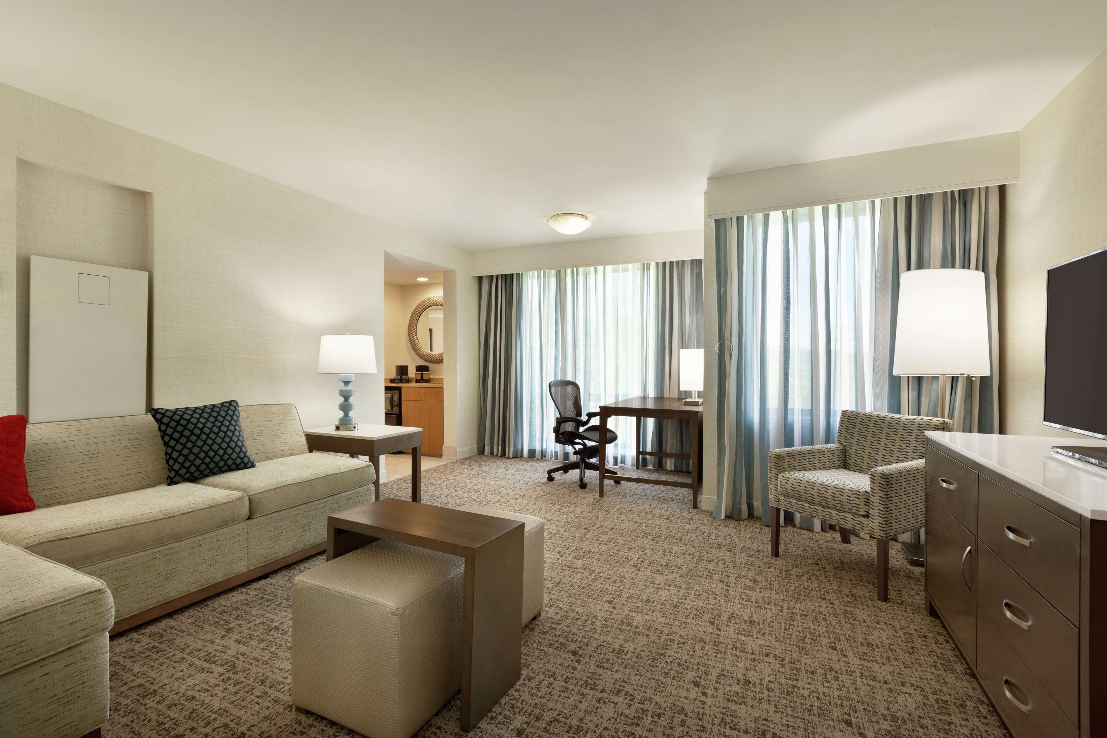 A hotel room with a sofa, armchair, desk, and a TV.