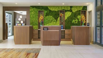 A reception area with two wooden reception desks, a green wall with a leaf pattern, and a visible Hilton sign.