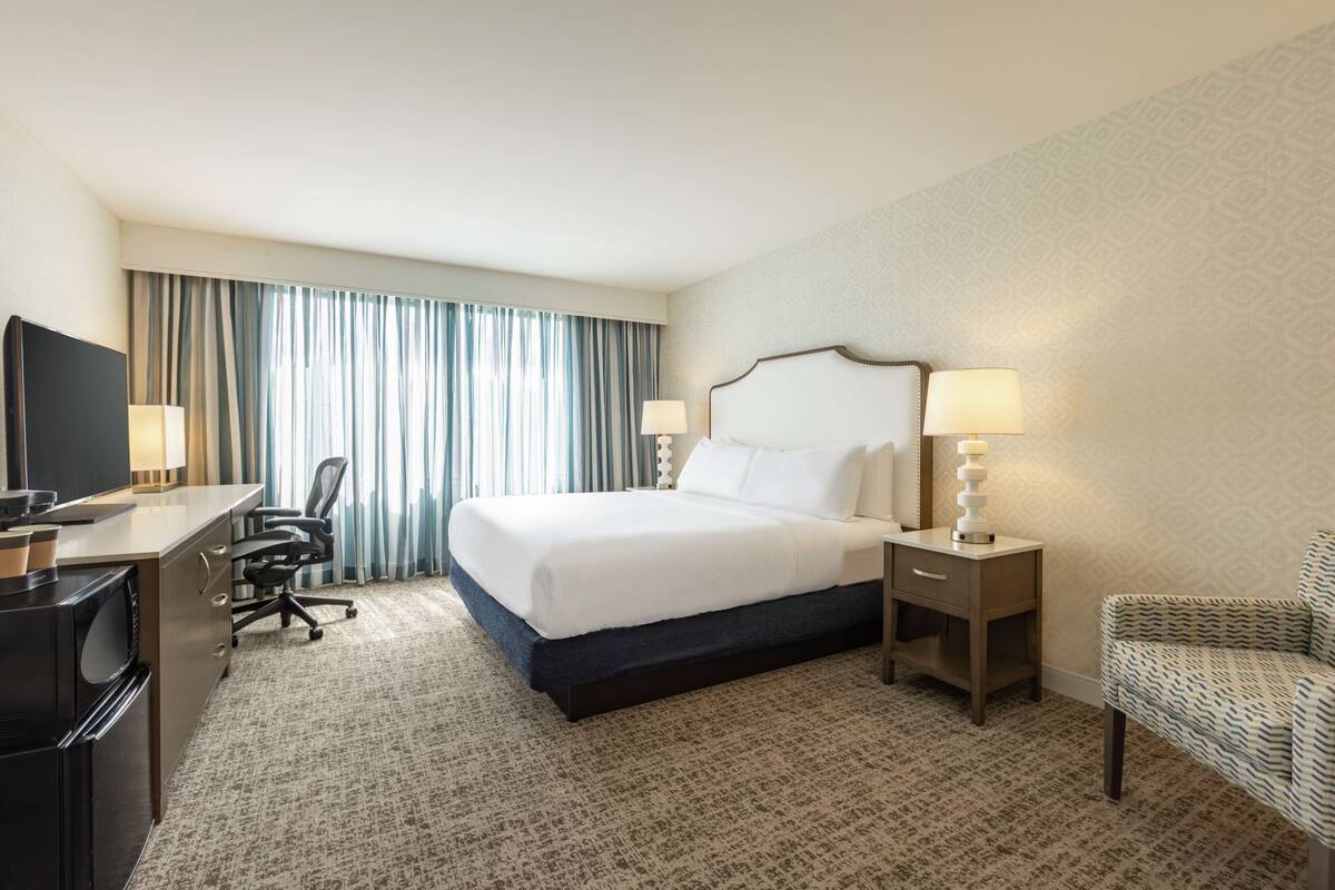 A hotel room with a bed, desk, chair, and two bedside lamps.