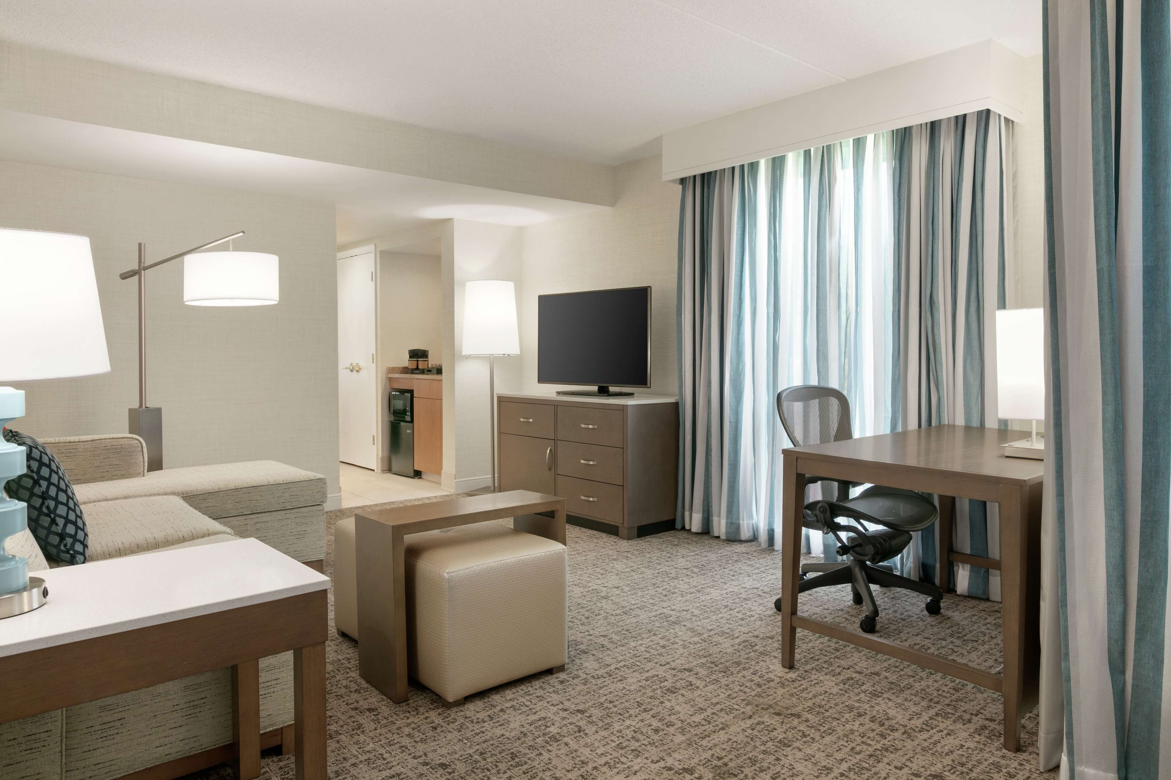 A hotel room with a bed, a desk with a chair, a television, and a bathroom visible in the background.