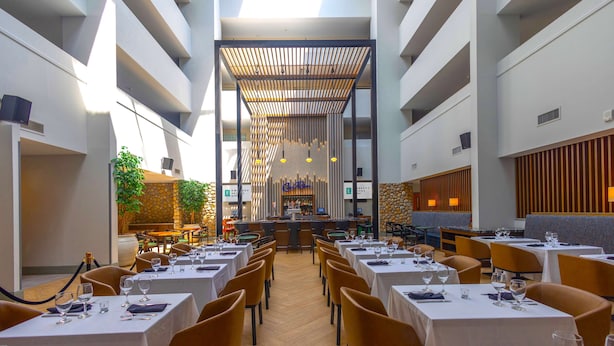 A restaurant with multiple dining tables and chairs, a bar area, and a central seating area with a wooden ceiling. - Embassy Suites by Hilton Philadelphia Valley Forge (Wayne)
