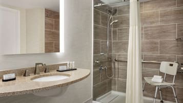 A modern bathroom with a granite countertop sink, a glass shower enclosure, and a white chair.
