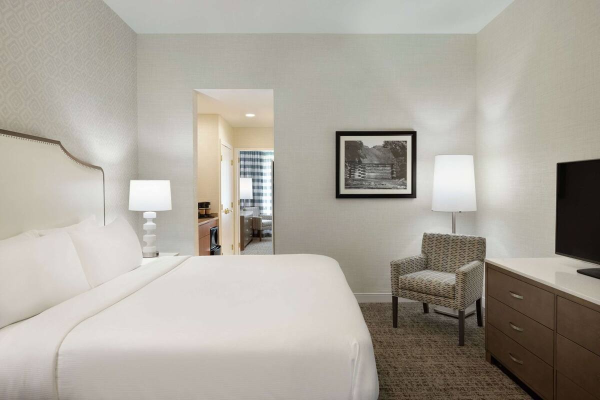 A hotel room with a large bed, a chair, a desk, a television, and a framed picture on the wall.