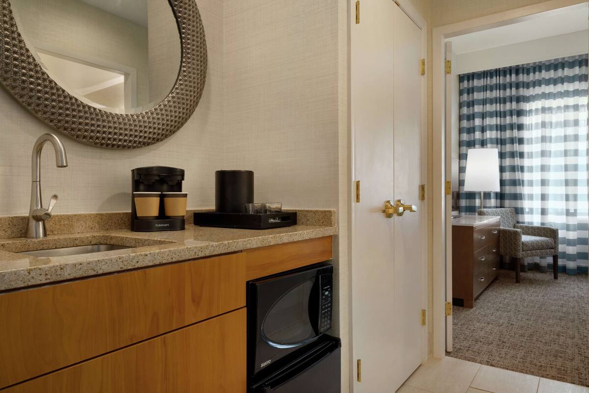 A modern bathroom with a sink, coffee maker, microwave, and a large mirror.