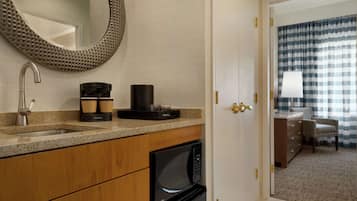 Un baño moderno con lavabo, cafetera, microondas y un espejo grande.