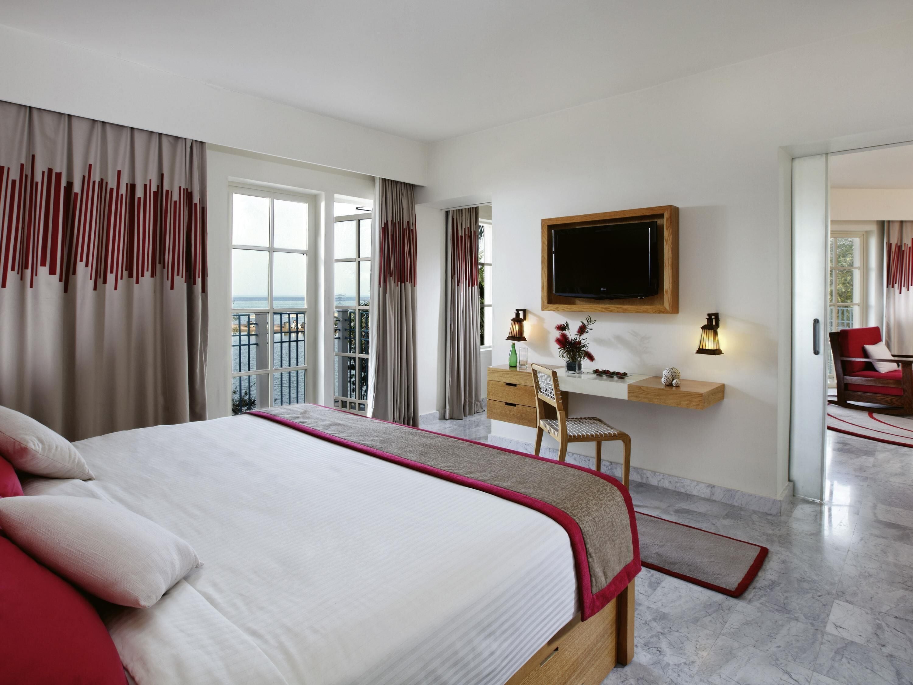 A hotel room with a bed, a desk, a TV, and a balcony with a view.