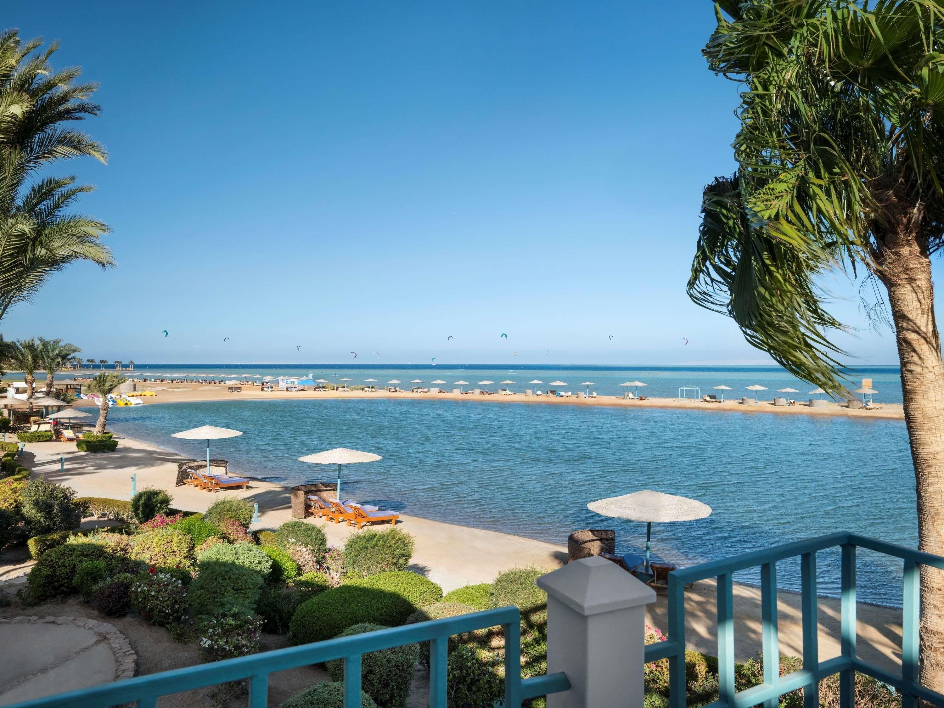 Ett semesterhotell vid stranden med solstolar, parasoller och utsikt över havet.