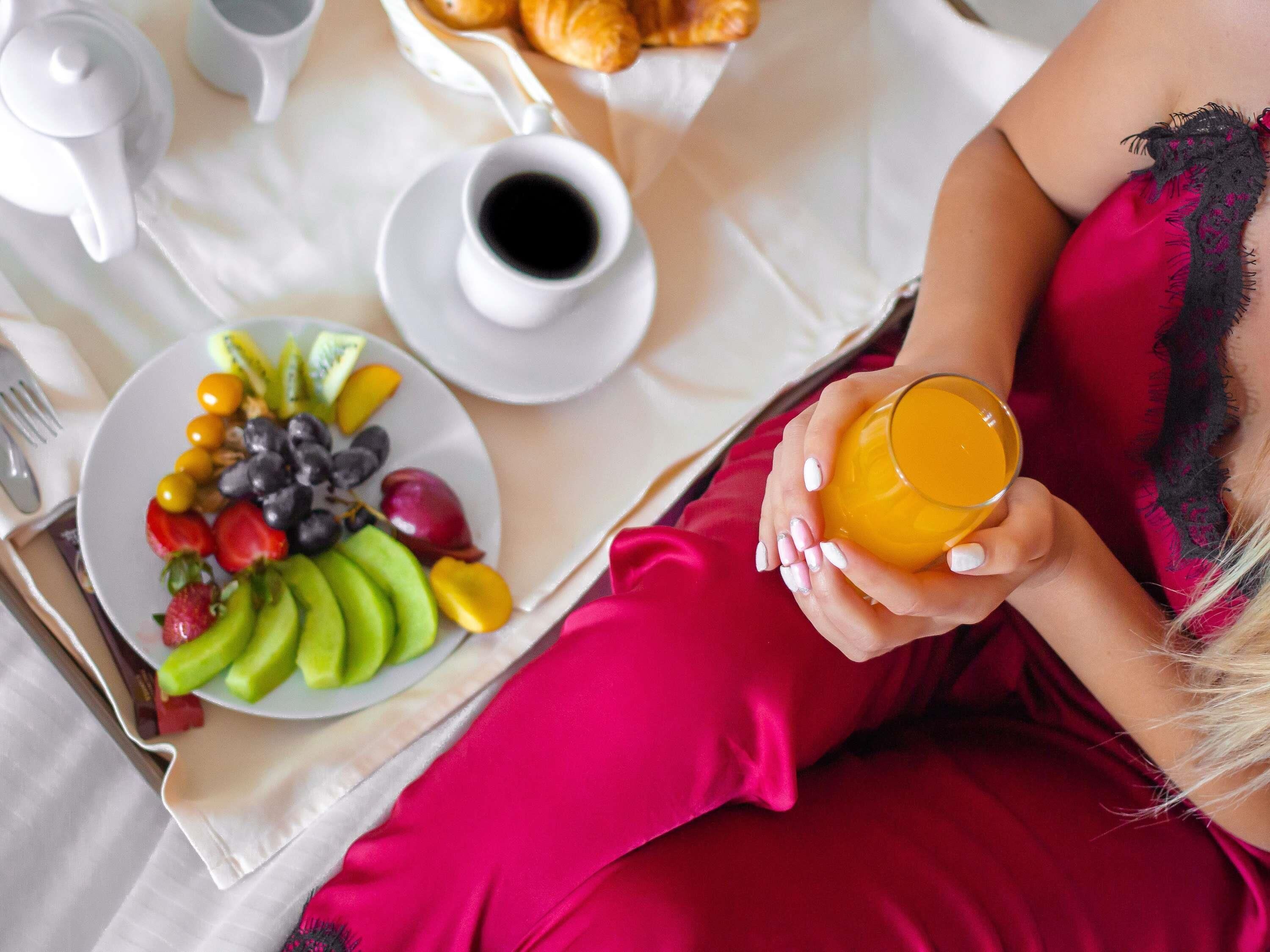 A breakfast tray with a plate of fruit, a cup of coffee, and a glass of orange juice.