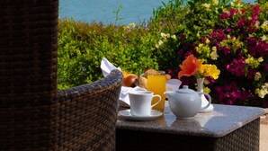 A wicker chair and table with breakfast items, a view of the beach, and umbrellas.