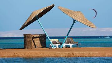 Una playa con dos sombrillas de paja y sillones reclinables.