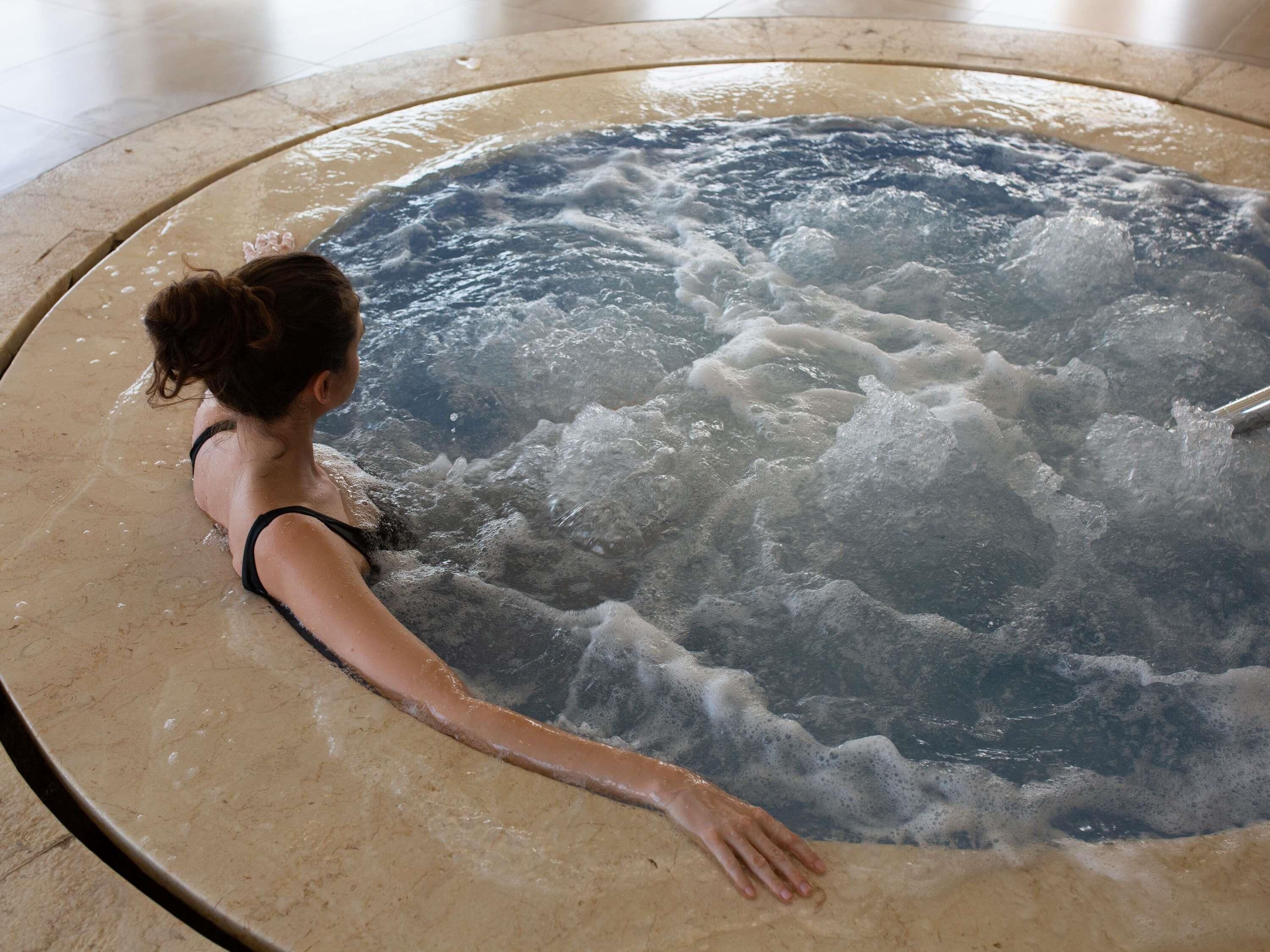 Una persona relajándose en un jacuzzi con piso de mármol.