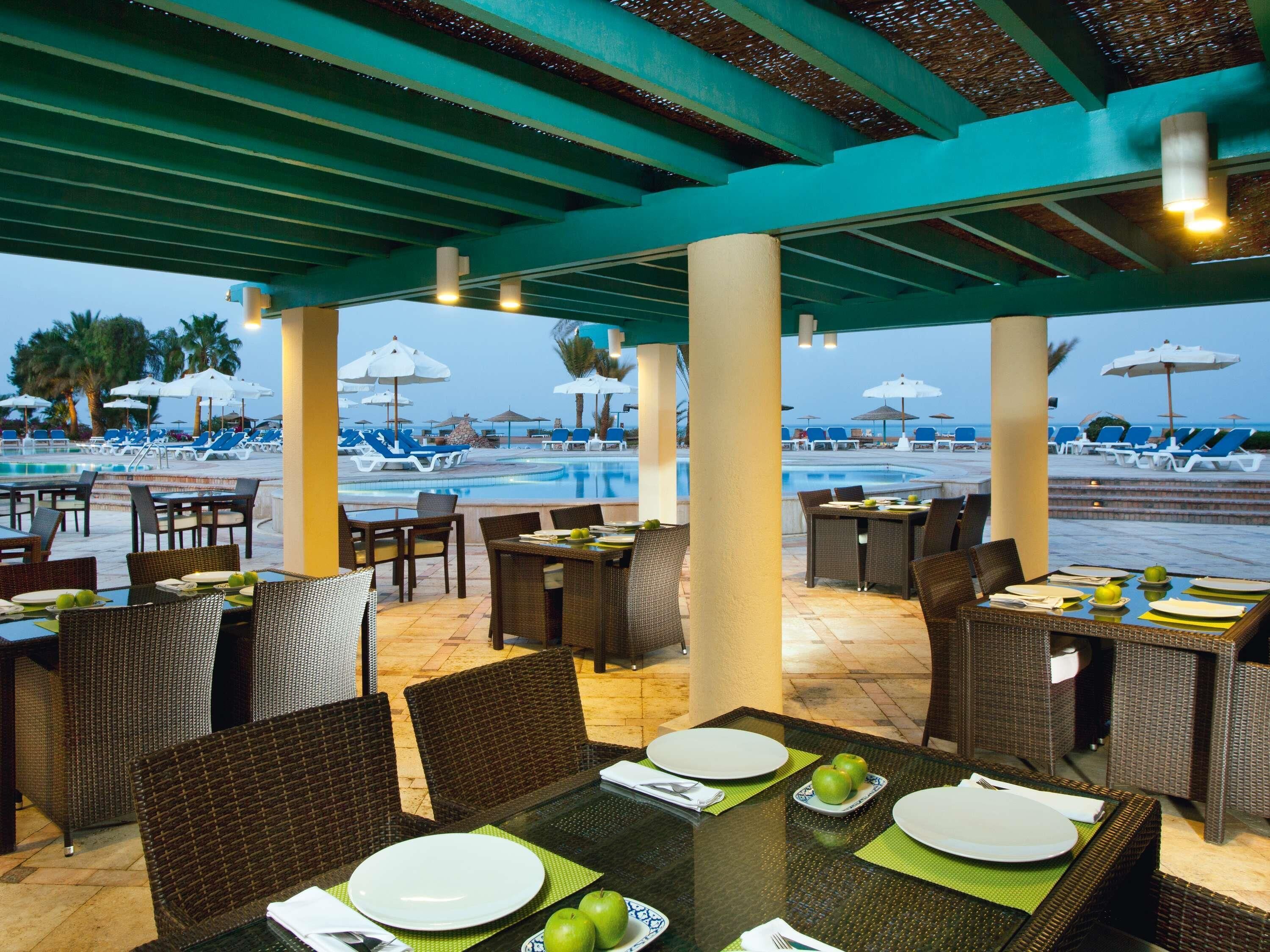 An outdoor dining area with tables and chairs, overlooking a pool and beach.